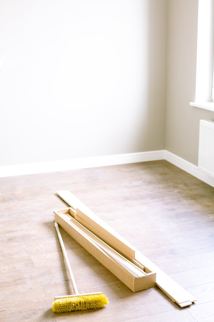 services-03 An empty room with wood planks and a broom, ready for renovation.